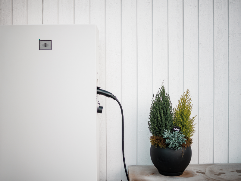 Batterilagring 1 Närbild på Emaldo hembatteri i Täby – anslutet och installerat intill yttervägg med dekorativa växter.